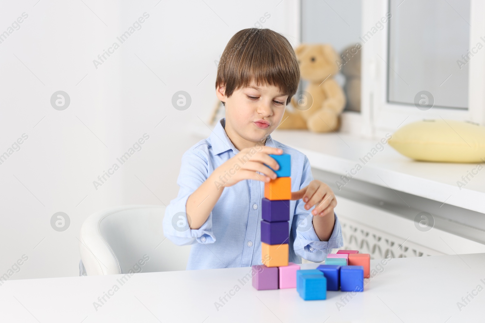 Photo of Boy building tower of colorful cubes at table indoors