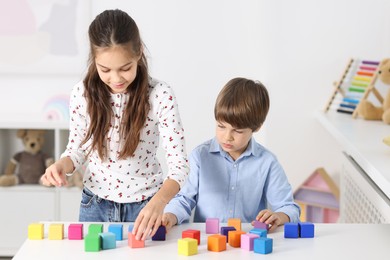 Photo of Children playing with colorful cubes at table indoors