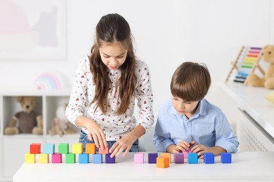 Children playing with colorful cubes at table indoors