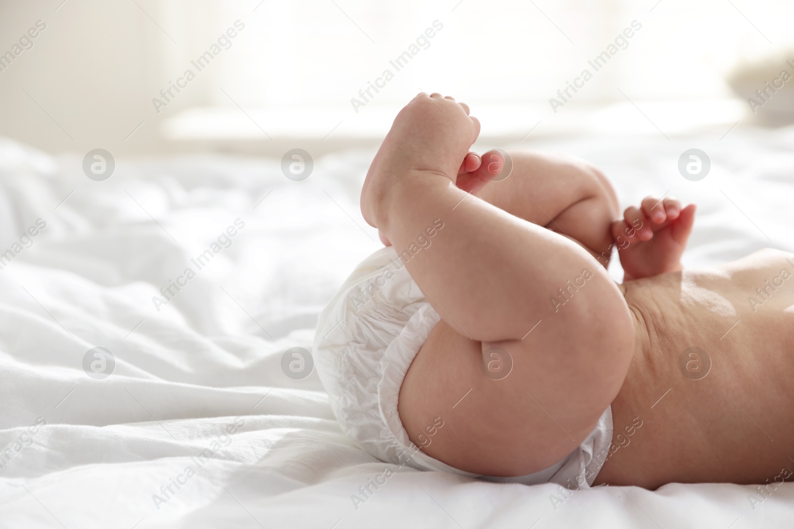 Photo of Cute little baby in diaper on bed indoors, closeup