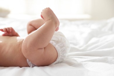 Photo of Cute little baby in diaper on bed indoors, closeup