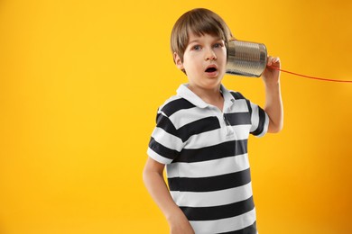 Photo of Boy using tin can telephone on yellow background, space for text