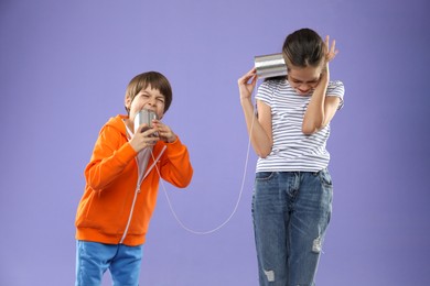 Girl and boy talking on tin can telephone against violet background