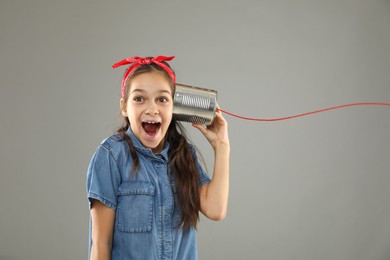 Girl using tin can telephone on gray background