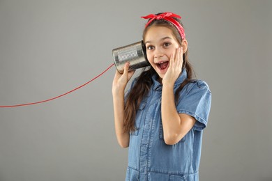 Girl using tin can telephone on gray background