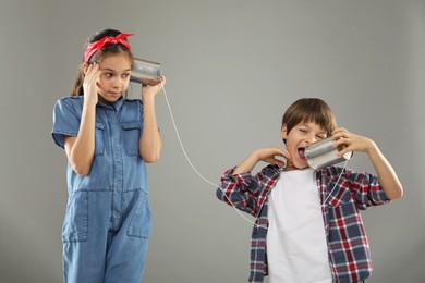 Photo of Girl and boy talking on tin can telephone against gray background