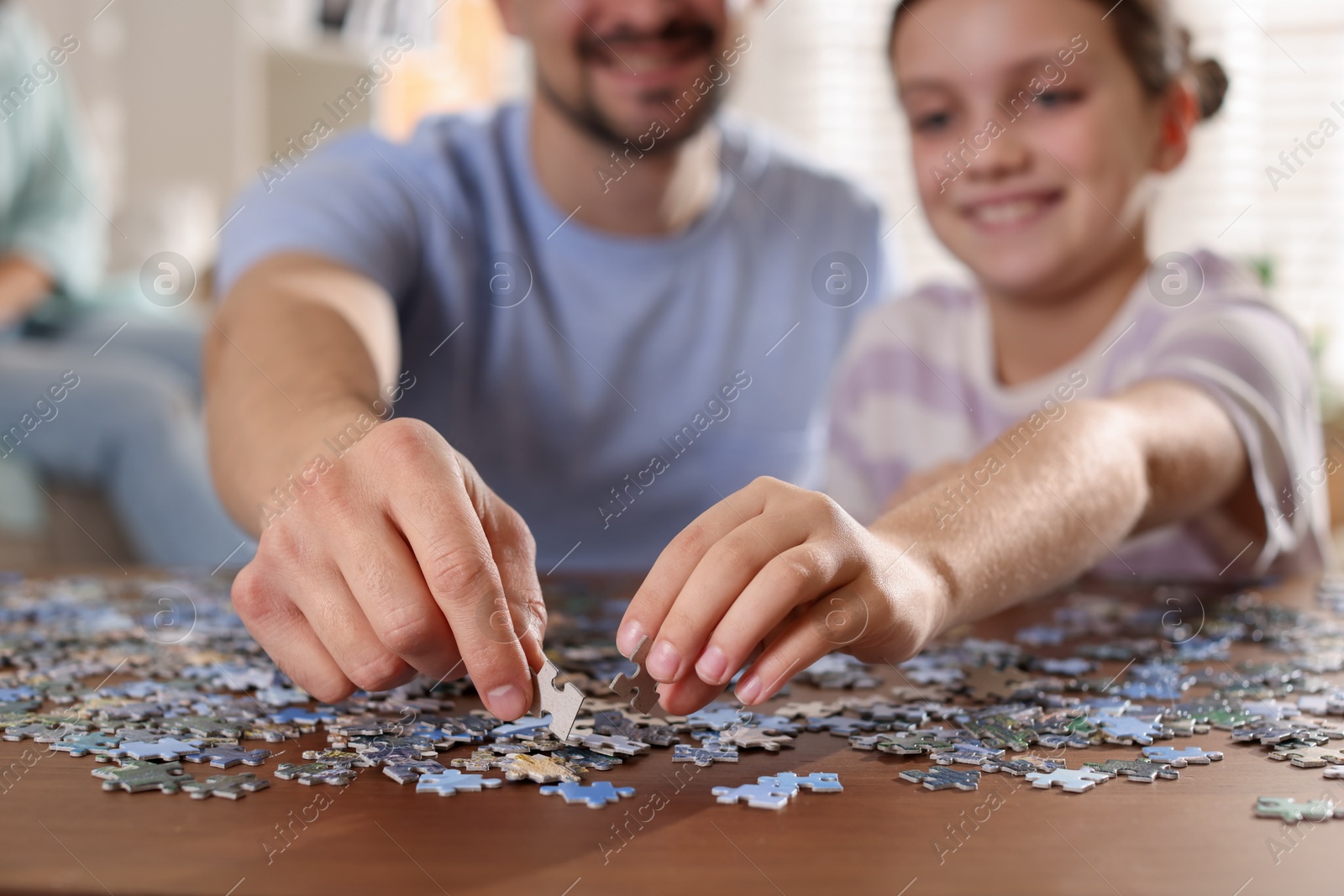 Photo of Happy father and his daughter solving puzzle together at wooden table indoors, selective focus