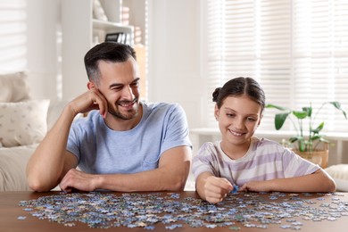 Photo of Happy father and his daughter solving puzzle together at wooden table indoors