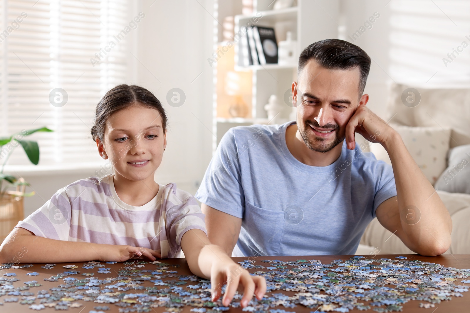 Photo of Happy father and his daughter solving puzzle together at wooden table indoors