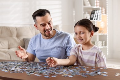 Photo of Happy father and his daughter solving puzzle together at wooden table indoors