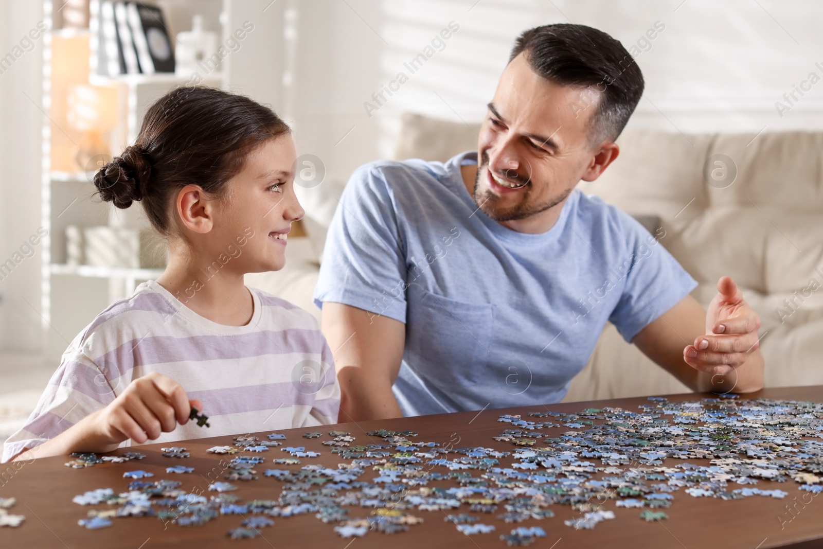 Photo of Happy father and his daughter solving puzzle together at wooden table indoors