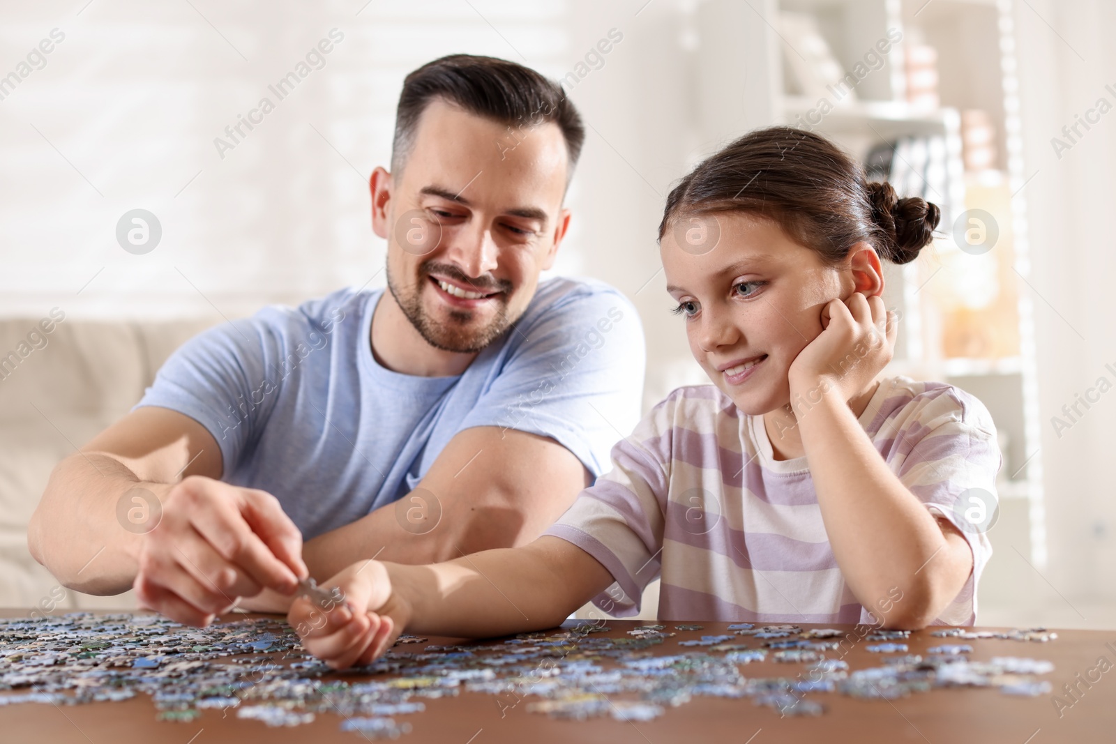 Photo of Happy father and his daughter solving puzzle together at wooden table indoors