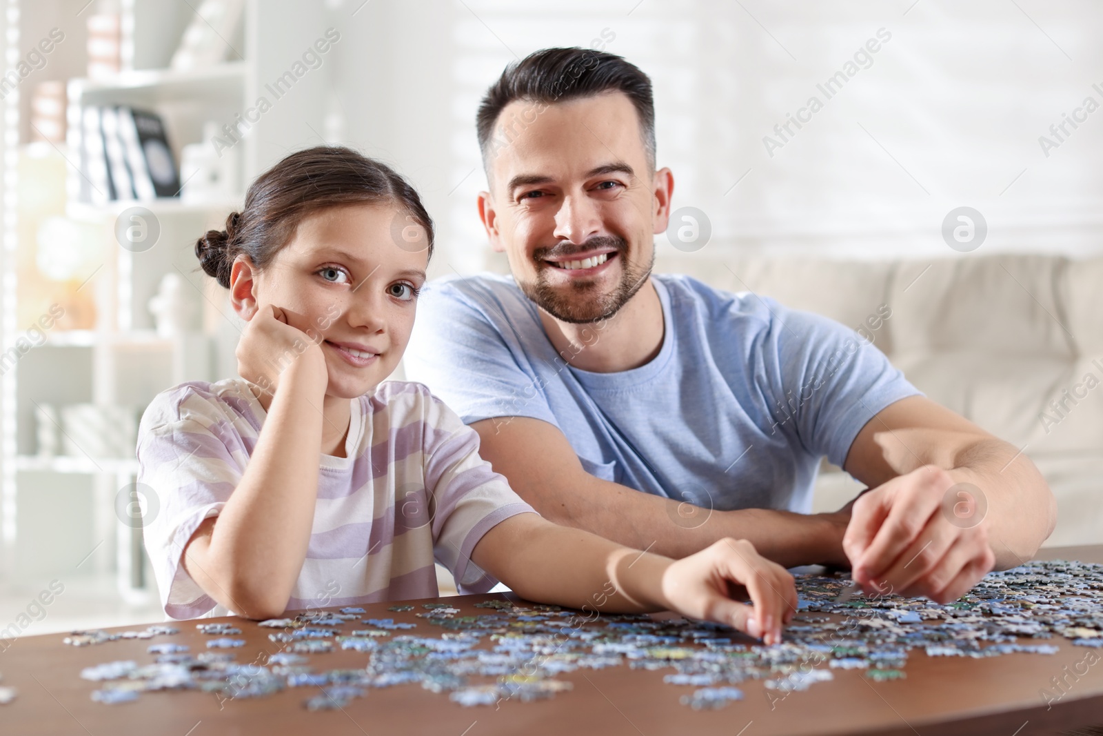 Photo of Happy father and his daughter solving puzzle together at wooden table indoors