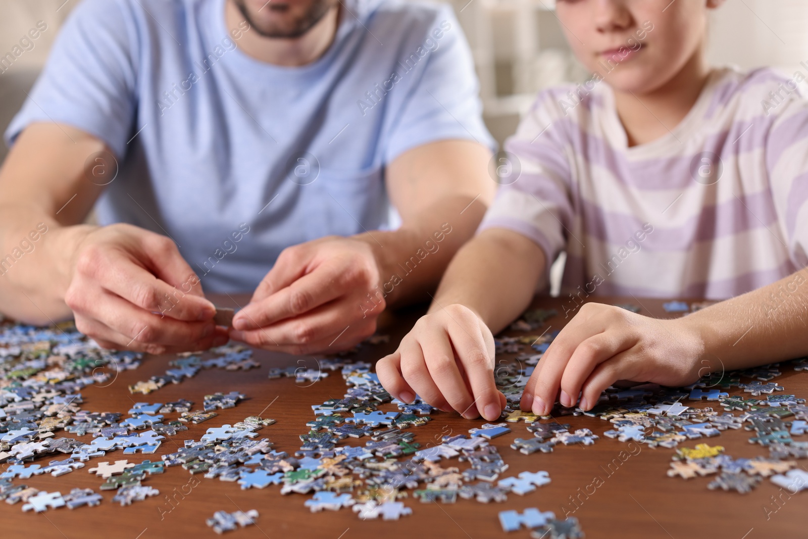 Photo of Father and his daughter solving puzzle together at wooden table indoors, closeup