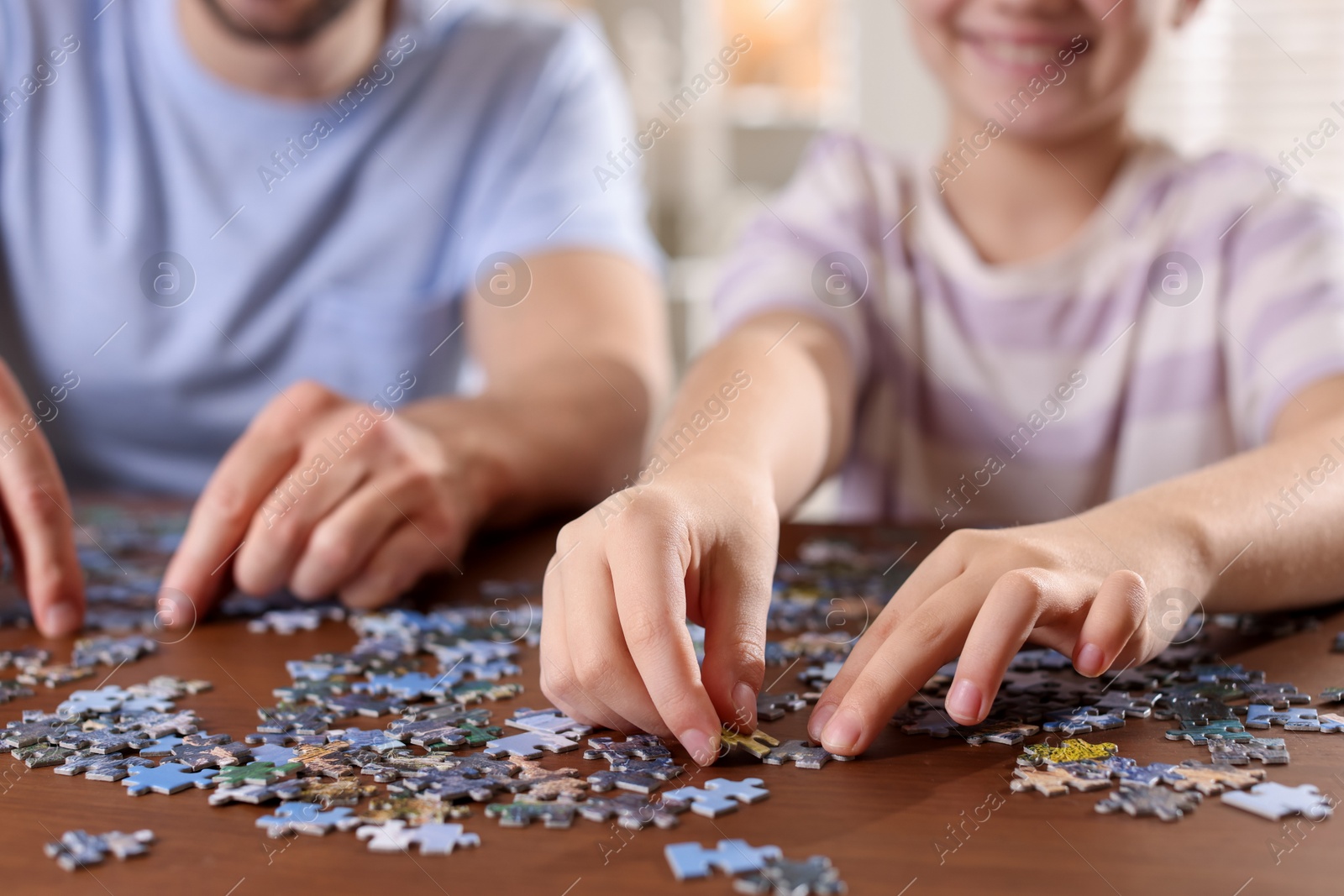 Photo of Father and his daughter solving puzzle together at wooden table indoors, closeup