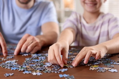 Photo of Father and his daughter solving puzzle together at wooden table indoors, closeup