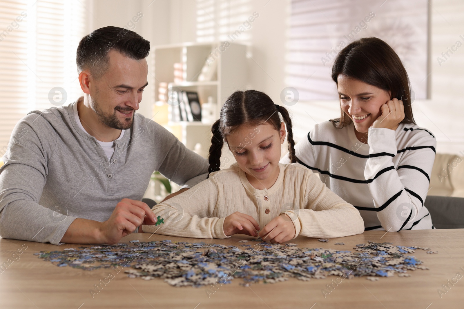 Photo of Happy parents and their daughter solving puzzle together at wooden table indoors