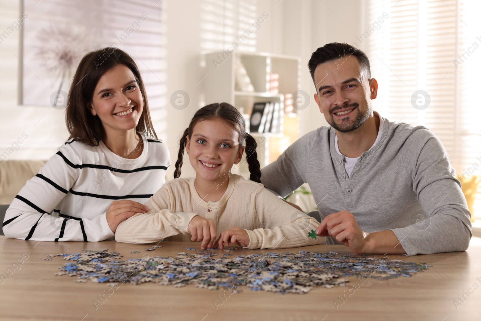 Photo of Happy parents and their daughter solving puzzle together at wooden table indoors