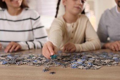 Photo of Happy parents and their daughter solving puzzle together at wooden table indoors, closeup