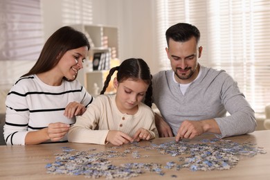 Photo of Happy parents and their daughter solving puzzle together at wooden table indoors