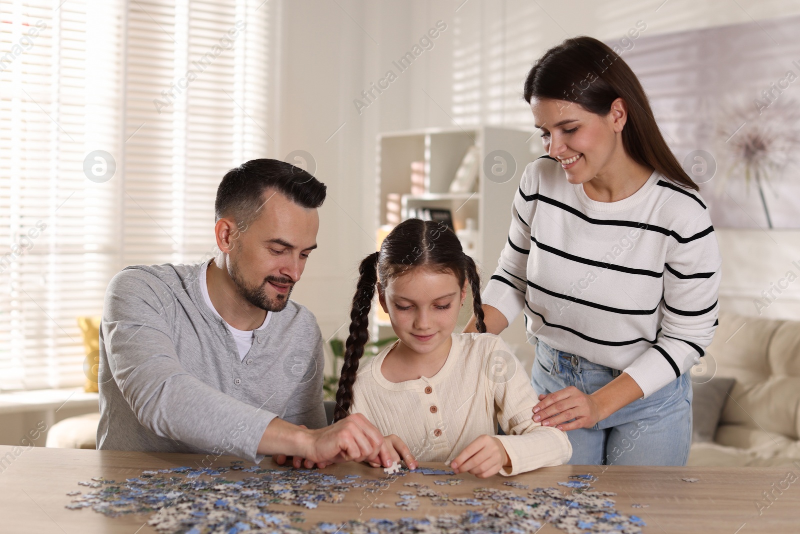 Photo of Happy parents and their daughter solving puzzle together at wooden table indoors