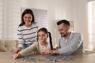 Photo of Happy parents and their daughter solving puzzle together at wooden table indoors