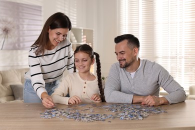 Photo of Happy parents and their daughter solving puzzle together at wooden table indoors