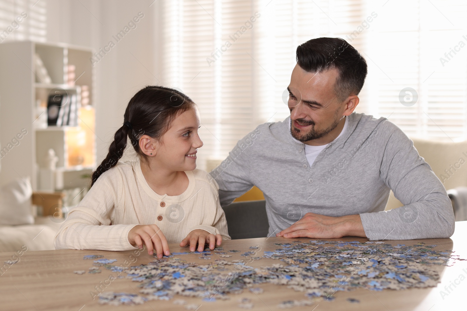 Photo of Happy father and his daughter solving puzzle together at wooden table indoors