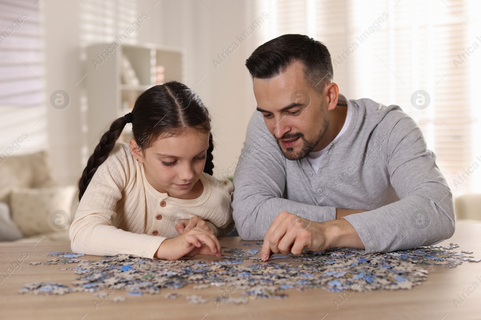 Photo of Happy father and his daughter solving puzzle together at wooden table indoors