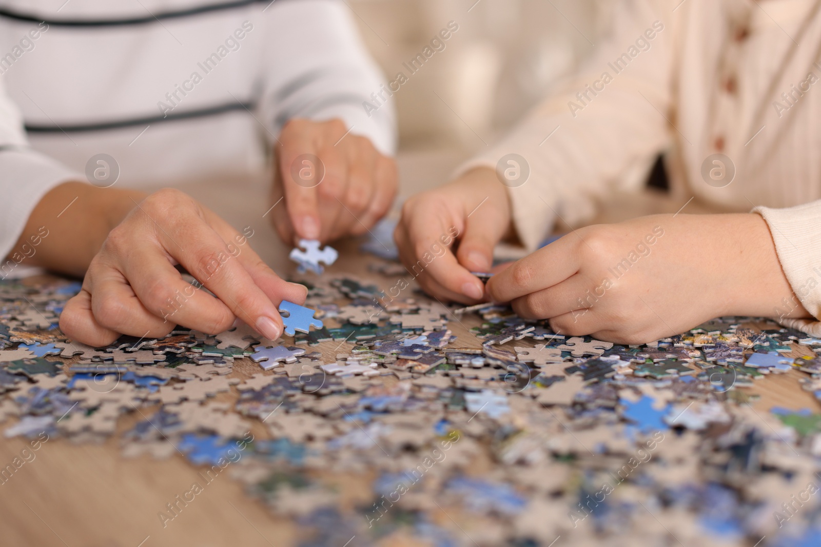 Photo of Mother and her daughter solving puzzle together at wooden table indoors, closeup