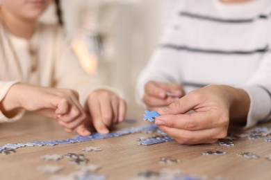 Photo of Mother and her daughter solving puzzle together at wooden table indoors, closeup