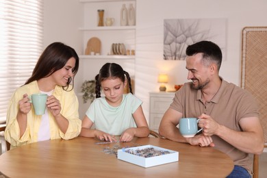 Photo of Happy parents and their daughter solving puzzle together at wooden table indoors