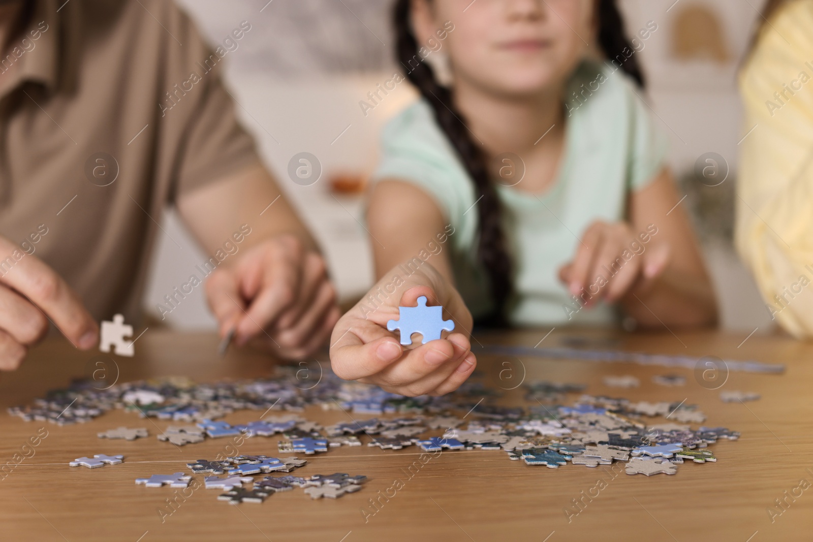 Photo of Parents and their daughter solving puzzle together at wooden table indoors, closeup