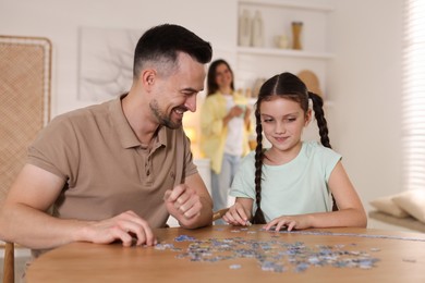 Photo of Happy father and his daughter solving puzzle together at wooden table indoors, selective focus