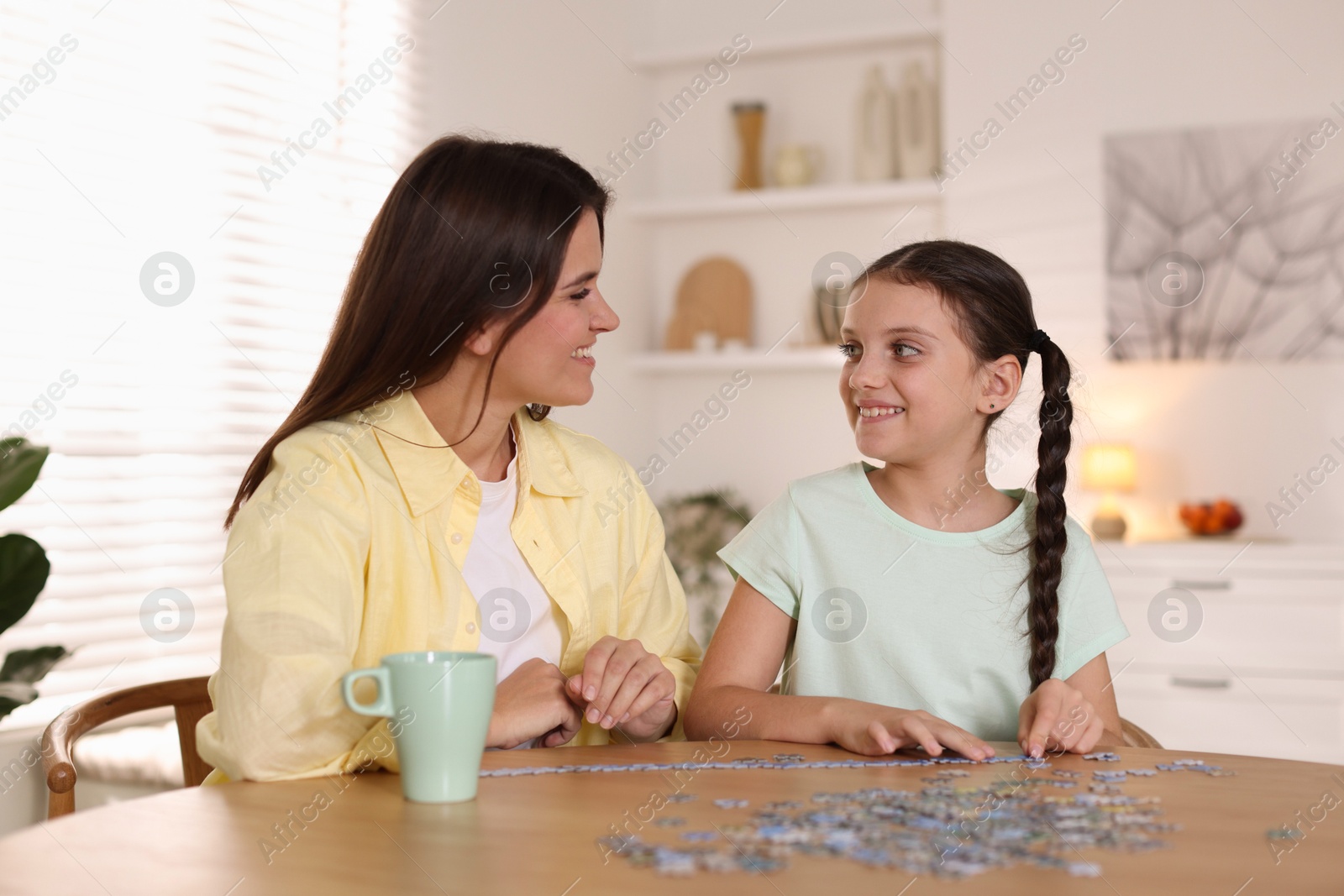 Photo of Happy mother and her daughter solving puzzle together at wooden table indoors