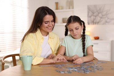 Photo of Happy mother and her daughter solving puzzle together at wooden table indoors