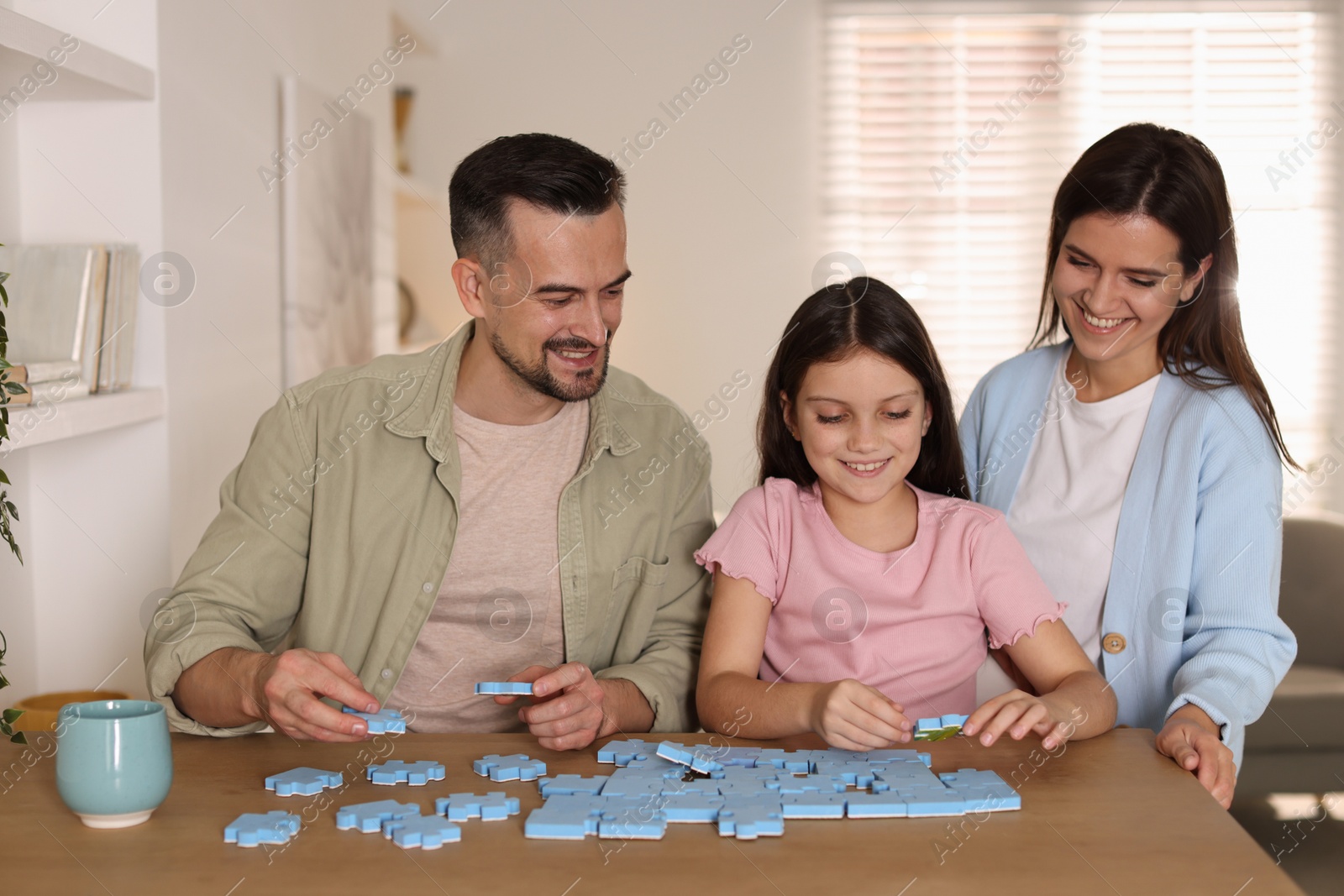 Photo of Happy parents and their daughter solving puzzle together at wooden table indoors