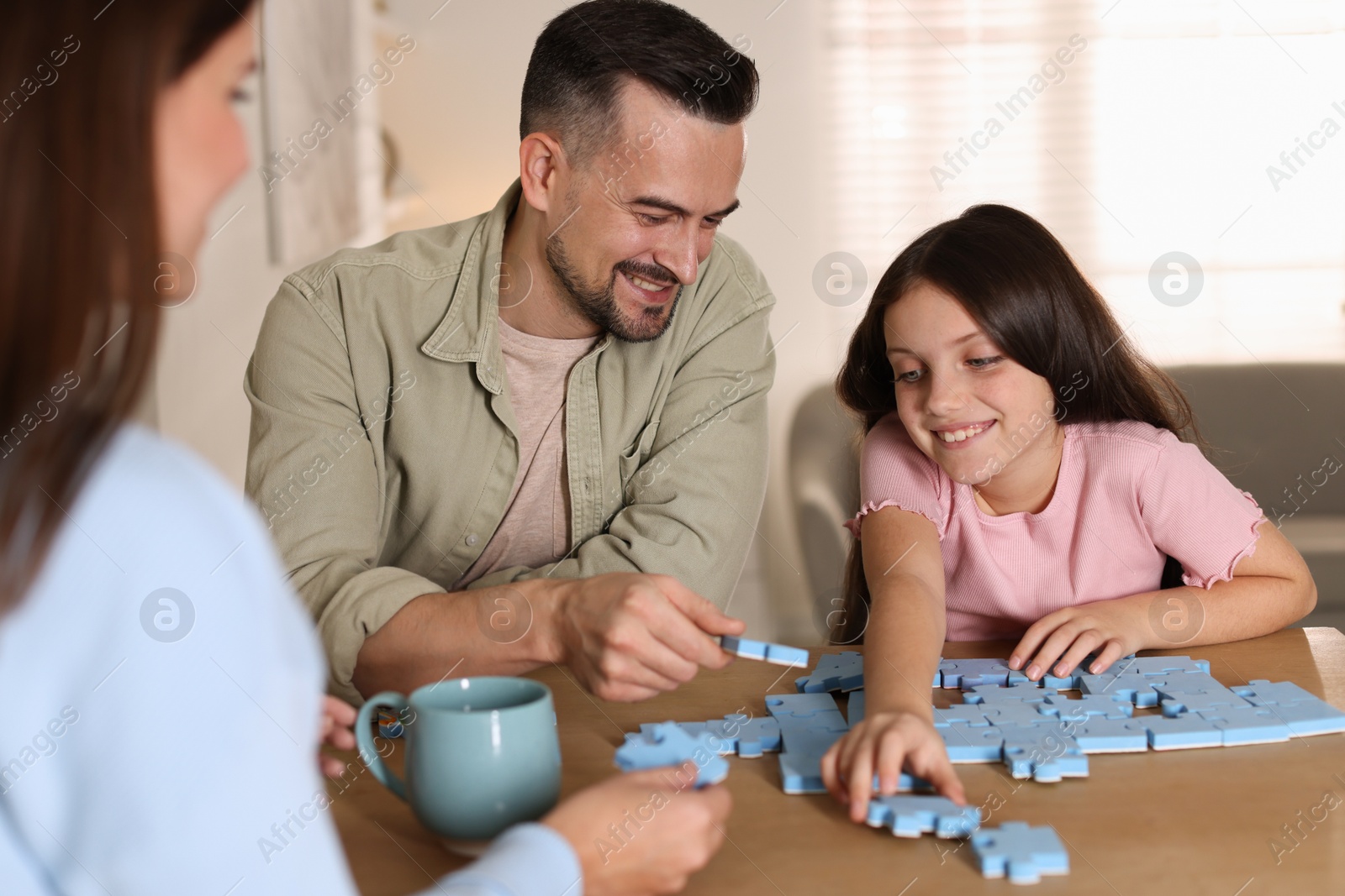 Photo of Happy parents and their daughter solving puzzle together at wooden table indoors