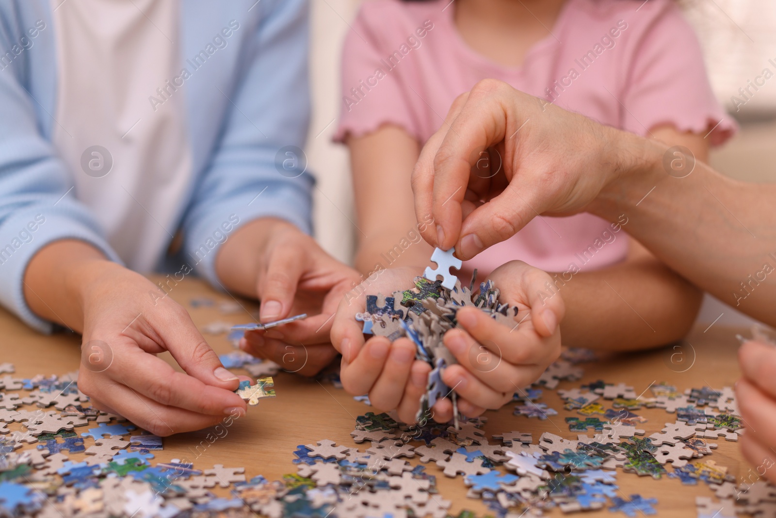 Photo of Parents and their daughter solving puzzle together at wooden table indoors, closeup