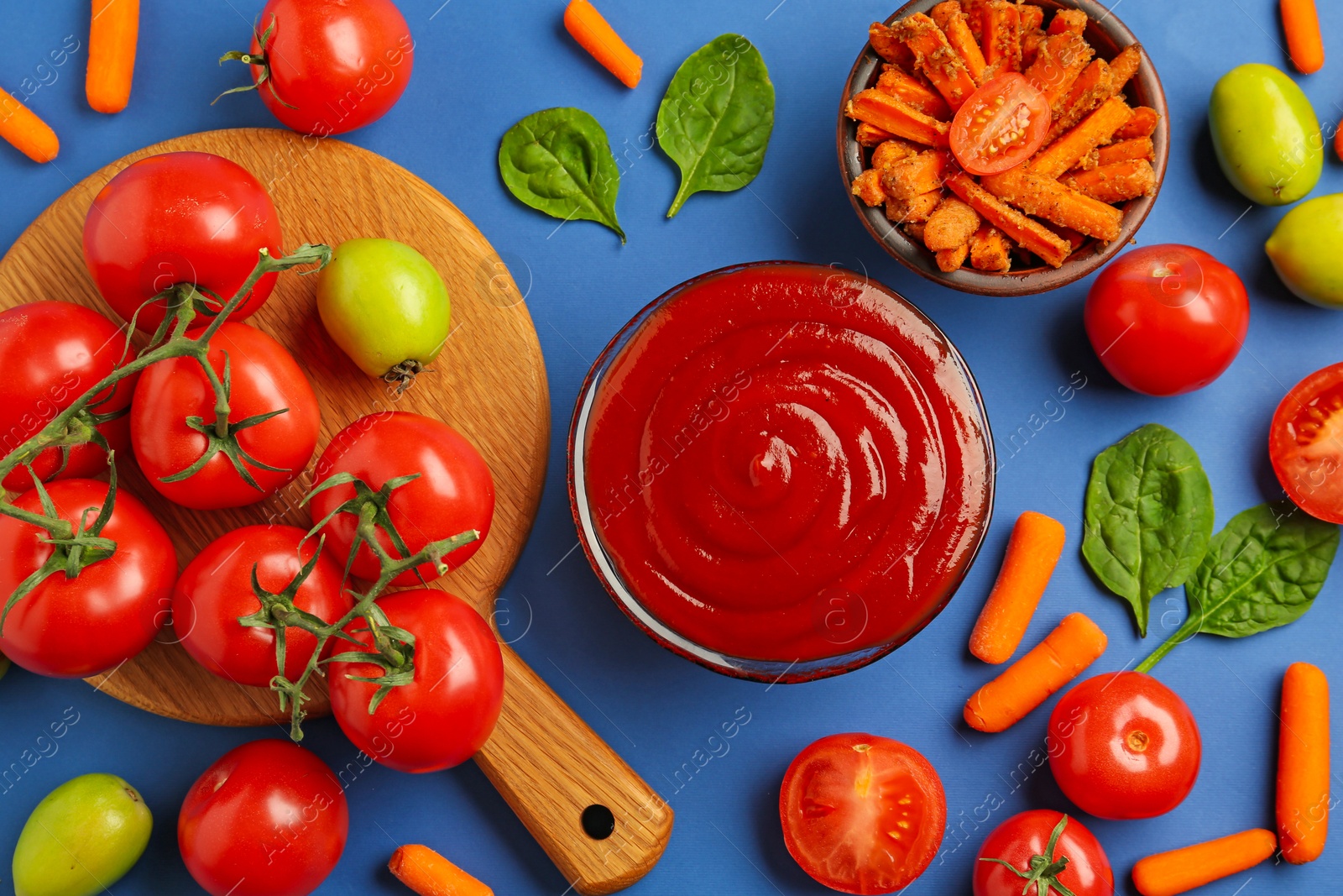 Photo of Tasty ketchup and vegetables on blue background, flat lay