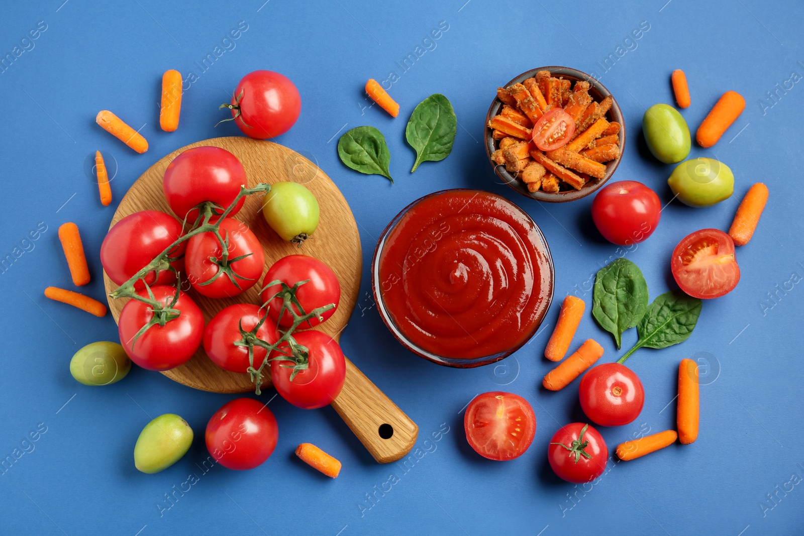 Photo of Tasty ketchup and vegetables on blue background, flat lay