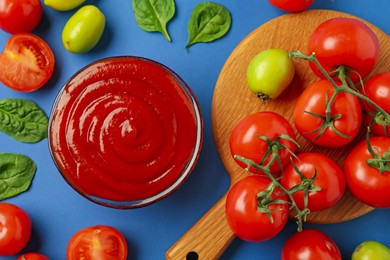 Photo of Tasty ketchup and vegetables on blue background, flat lay