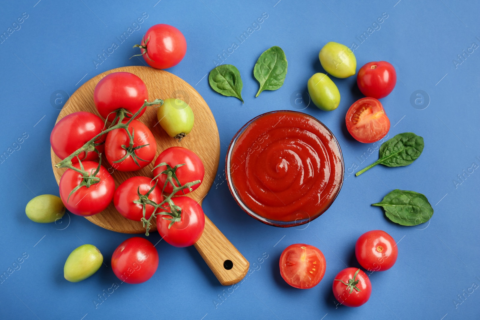 Photo of Tasty ketchup and vegetables on blue background, flat lay