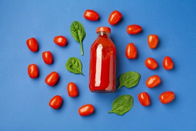 Photo of Tasty ketchup in bottle, tomatoes and basil on blue background, flat lay