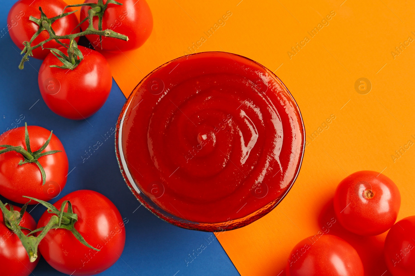 Photo of Tasty ketchup and tomatoes on color background, flat lay