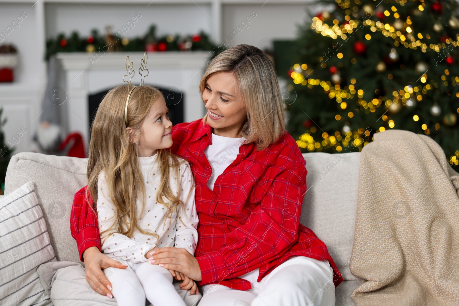 Photo of Cute little girl with her mom on sofa against Christmas lights