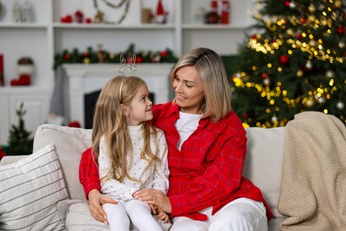 Cute little girl with her mom on sofa against Christmas lights