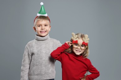 Funny children in Christmas accessories on grey background