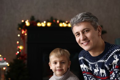 Photo of Dad and son near decorated fireplace at home, space for text. Christmas season