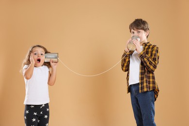 Photo of Boy and girl talking on tin can telephone against beige background